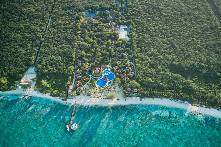 Aerial view of beachfront resort nestled in dense jungle with pools and turquoise waters
