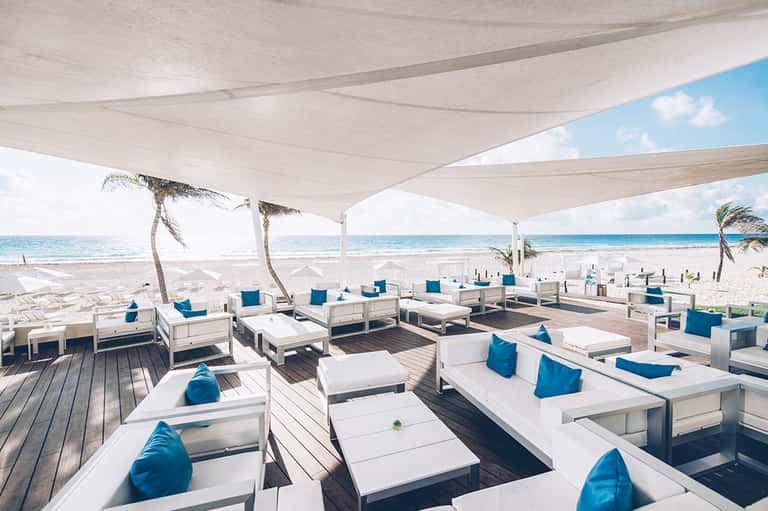 Beachfront lounge area with white daybeds, blue pillows, sailcloth canopy, and ocean views