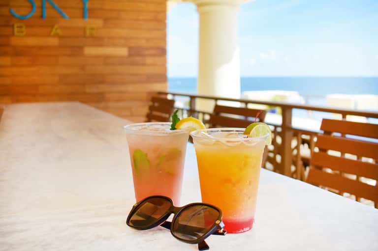 Two colorful tropical cocktails with lime garnish on a beachfront terrace overlooking the ocean