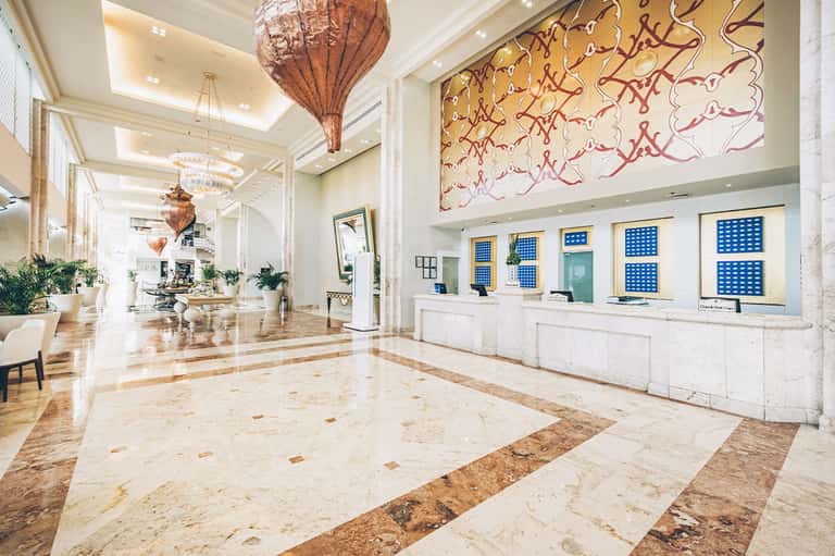 Luxurious hotel lobby with marble floors, decorative pendant lights, and artistic wall installations
