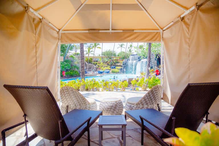 Glamping tent interior with comfortable seating overlooking a waterfall and tropical pool