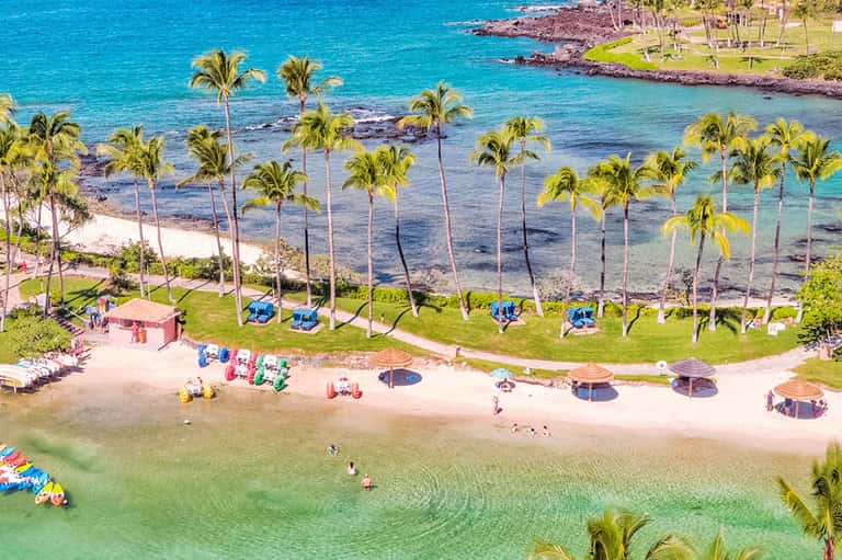 Aerial view of pristine beach with palm trees, turquoise water, and colorful beach umbrellas and loungers