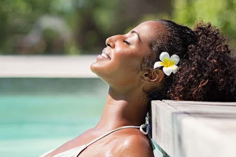 Woman relaxing by pool with white flower in hair and turquoise water