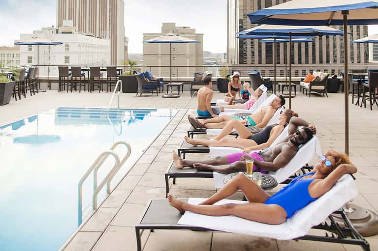 Urban rooftop pool with multiple guests lounging on chairs under blue umbrellas