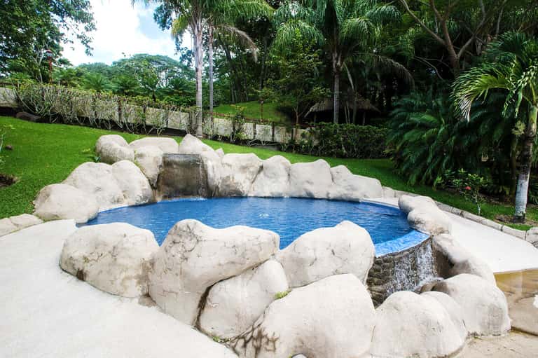 Natural hot spring pool surrounded by large white rocks in tropical garden setting