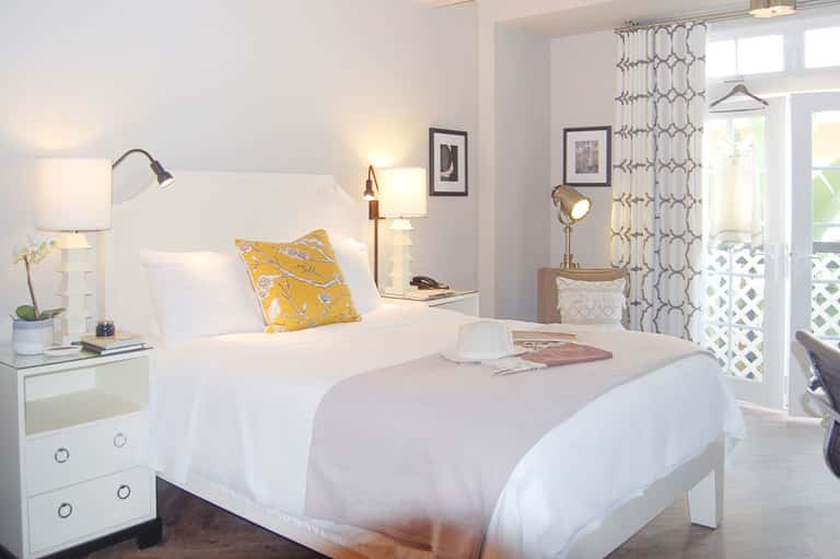 Modern hotel bedroom with white bedding, yellow accent pillow, and coastal balcony view