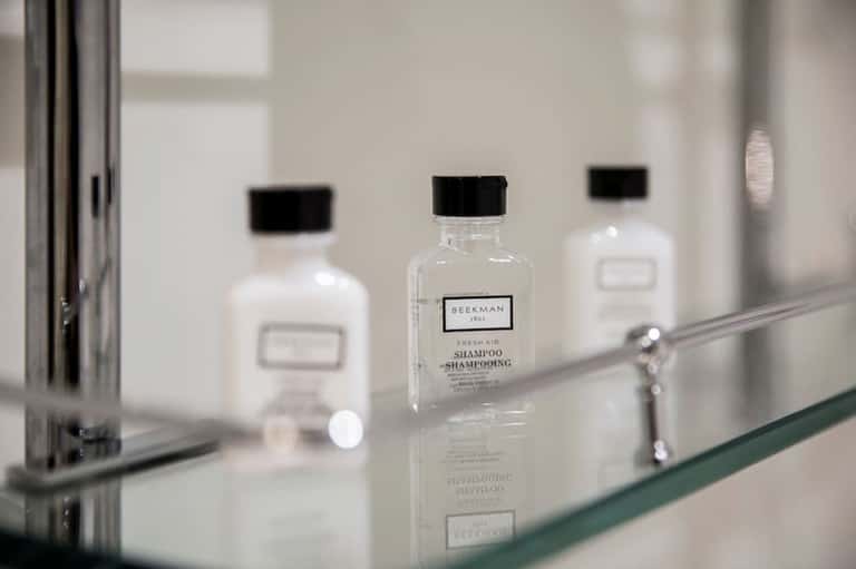 Bathroom counter displaying luxury Beekman toiletries in glass bottles with mirror reflection