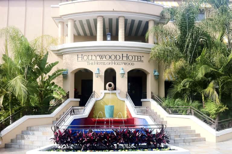 Historic Hollywood Hotel facade with palm trees and colorful fountain courtyard entrance