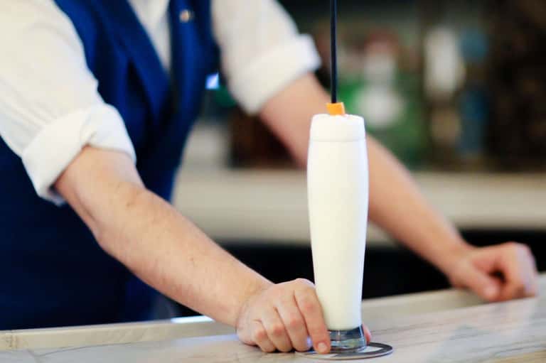 Bartender pouring white cocktail into tall glass with citrus garnish at resort bar