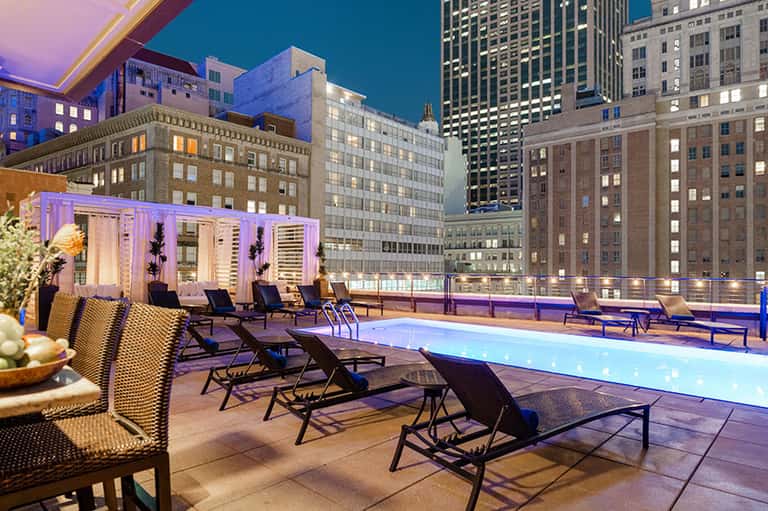 Rooftop pool at night with purple lighting, lounge chairs, and illuminated city skyline backdrop