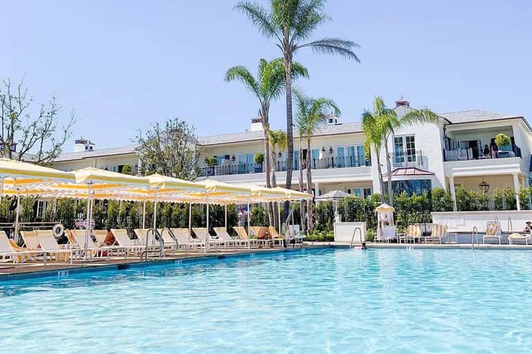 Resort pool area with white colonnade, yellow umbrellas, palm trees, and white buildings with balconies