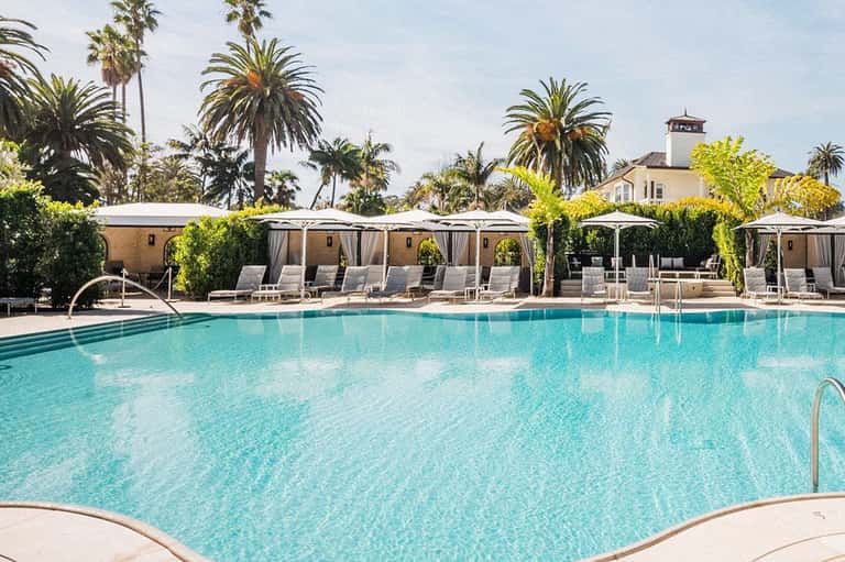 Resort swimming pool with lounge chairs, white umbrellas, and palm tree landscaping
