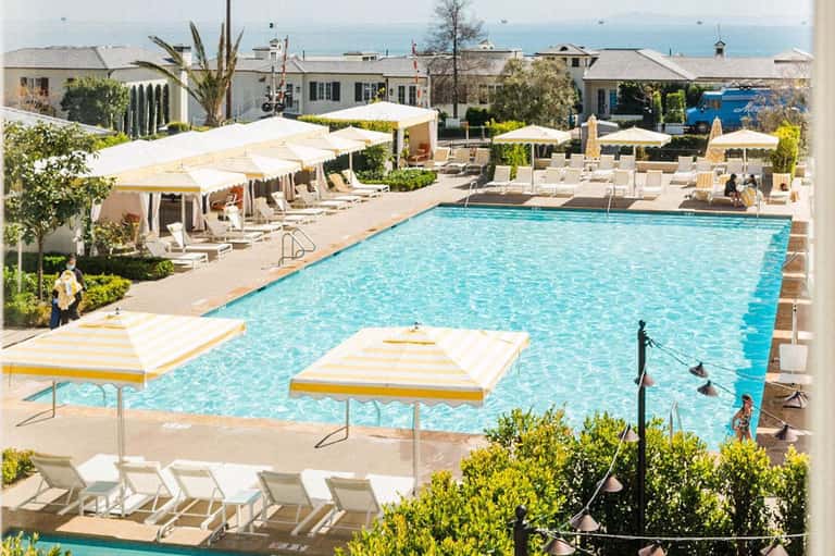 Resort swimming pool with yellow and white umbrellas, lounge chairs, and ocean view in background