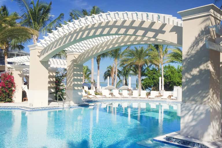 Luxury beachfront resort pool with white pergola, palm trees, and ocean view