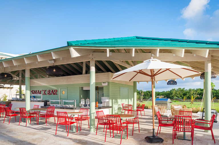 Snack bar pavilion with mint green roof, white columns, and red Adirondack chairs