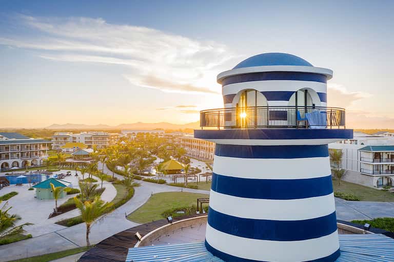 Striped lighthouse tower at sunset overlooking resort grounds and palm trees