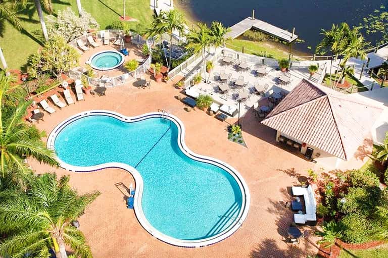 Aerial view of resort pools and lounge areas surrounded by palm trees and waterfront