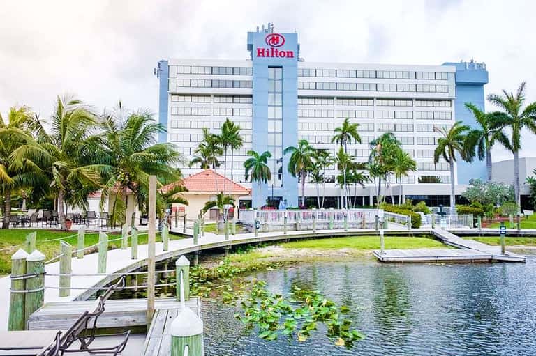Hilton hotel exterior with blue signage, palm trees, and waterfront dock area