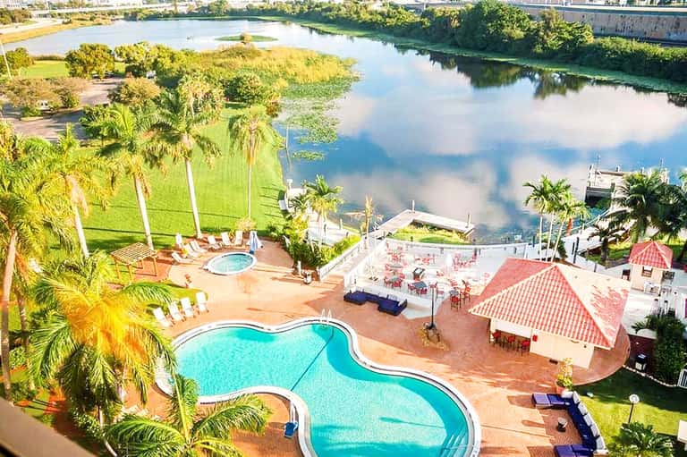 Aerial view of resort pool complex beside river with palm trees and event facilities