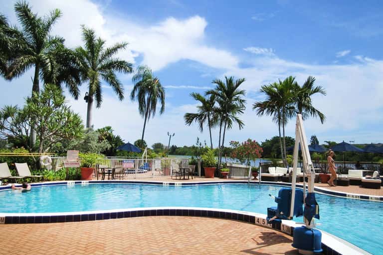 Resort pool with palm trees, lounge chairs, and umbrellas under blue sky