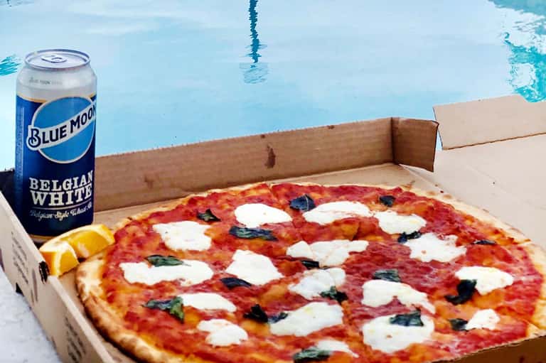 Margherita pizza with mozzarella and basil beside Blue Moon beer can at poolside