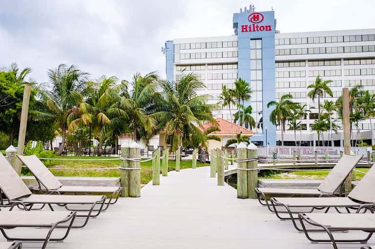Hilton hotel exterior with palm trees, wooden boardwalk, and lounge chairs by the water