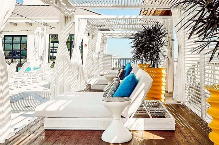 Modern white pergola lounge area with cushioned seating and ocean view from elevated deck