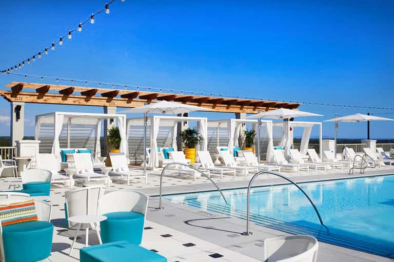 Modern poolside lounge area with white cabanas, pergola, and turquoise pool under clear sky