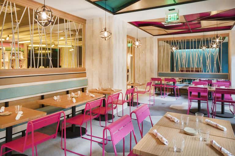 Contemporary restaurant interior with bright pink chairs, wooden tables, and geometric wall patterns