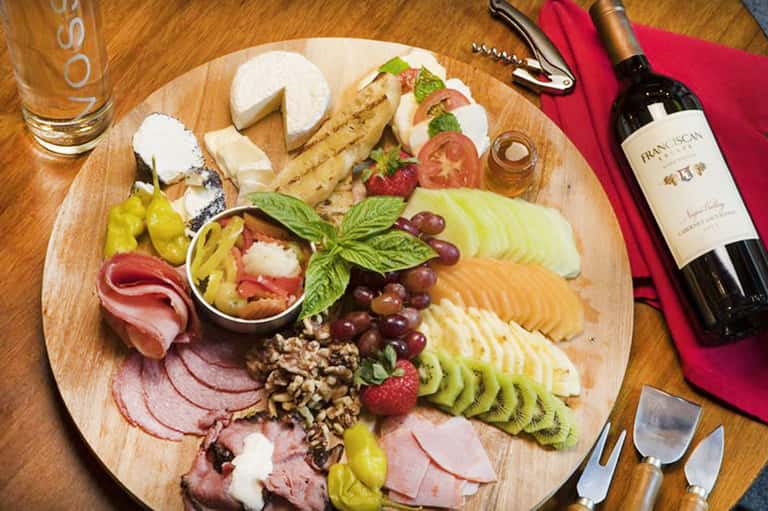 Charcuterie board with cured meats, cheeses, fruits, and wine bottle on table