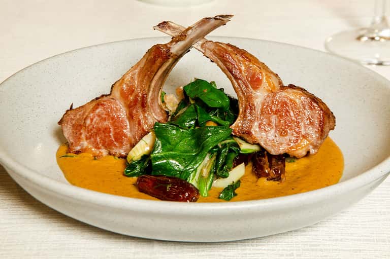 Plated lamb chops with sautéed greens and orange sauce on white ceramic dish