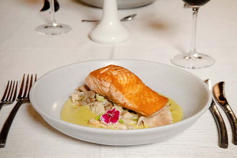 Gourmet plate with seared salmon fillet, rice, and garnish paired with wine glasses on white tablecloth