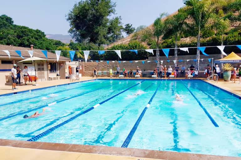 Olympic-sized lap pool with blue lane dividers and spectators under sunny skies