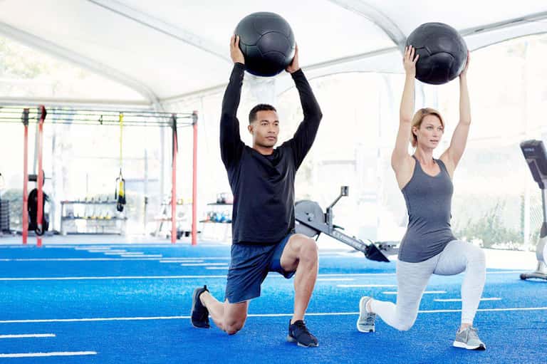 Two people performing medicine ball exercises in modern gym with blue floor