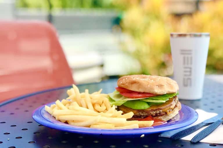 Burger and fries meal on blue plate by poolside with beverage cup and mountains in background