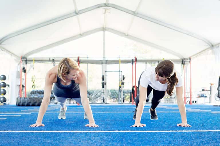 Two women exercising in a bright tent-covered fitness studio with equipment