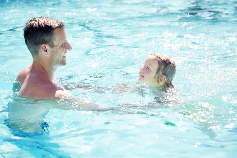 Adult and child swimming together in bright blue resort pool water
