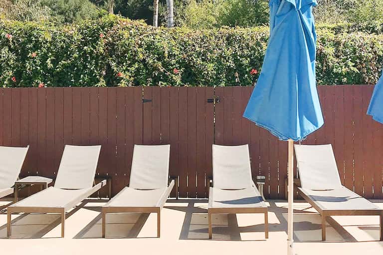 Beachside lounge chairs with blue umbrellas lined against a wooden fence