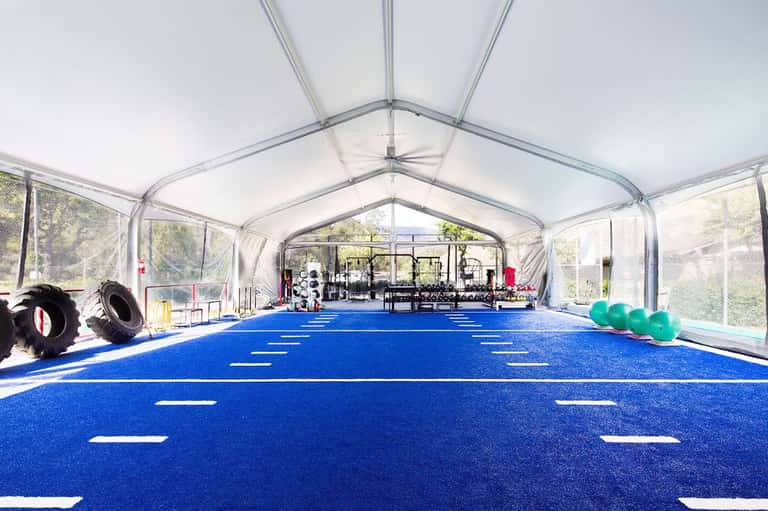 Clear-roofed indoor training facility with blue athletic flooring, exercise equipment, and green exercise balls