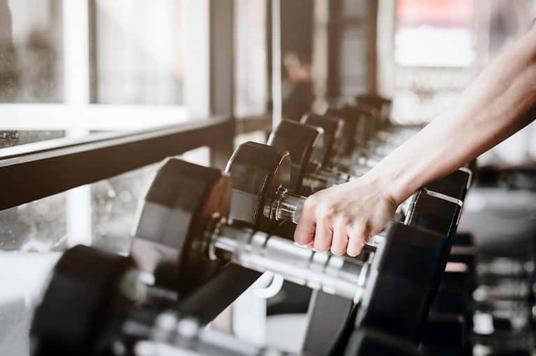 Person selecting a dumbbell from a row of weights in a bright fitness center gym