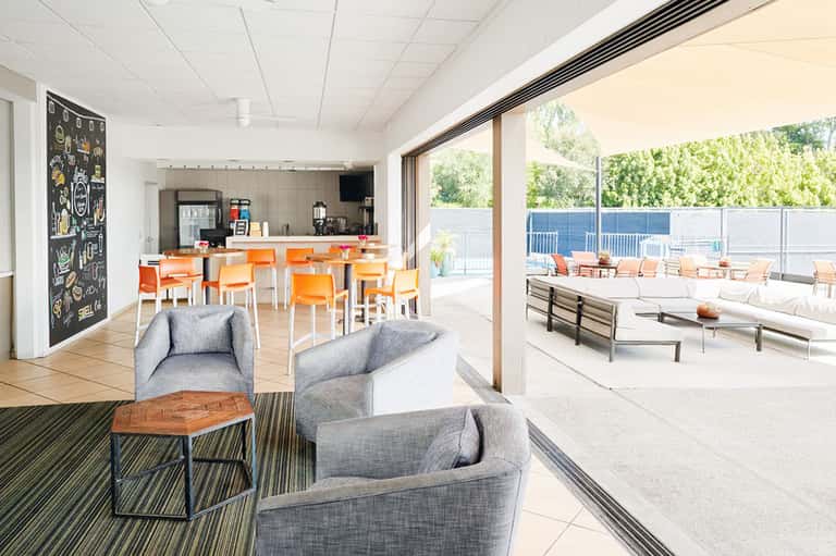Contemporary lounge with orange bar seating, gray armchairs, and outdoor terrace view