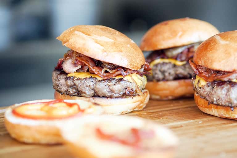 Gourmet bacon cheeseburgers with caramelized onions on wooden serving board