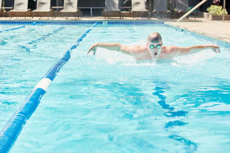Competitive swimmer doing butterfly stroke in Olympic-style lap pool with lane dividers