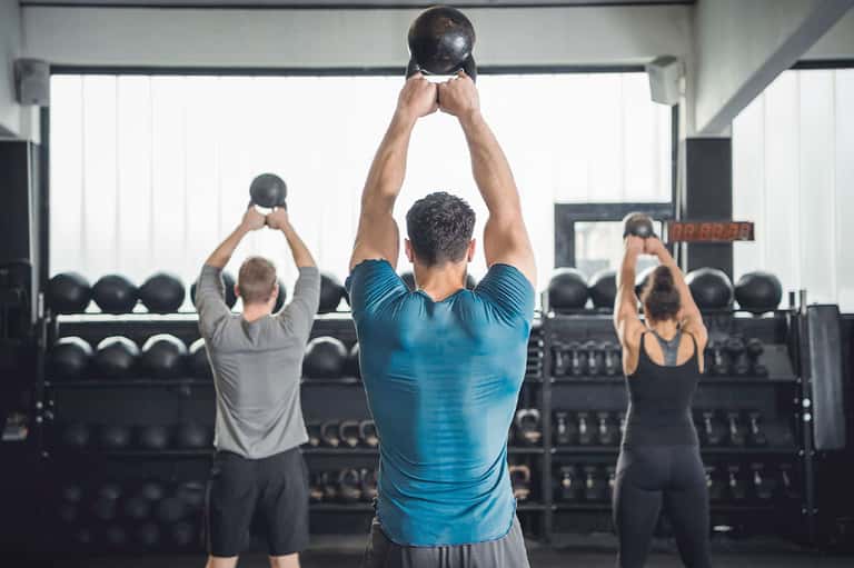 Fitness class with people performing kettlebell exercises in bright gym