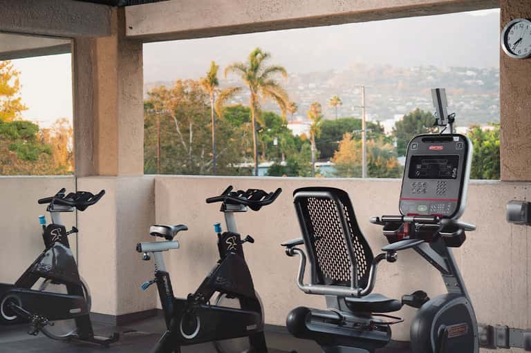 Rooftop fitness area with stationary bikes and elliptical machines overlooking hillside landscape