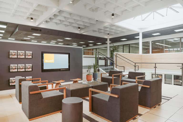 Modern hotel lobby lounge with gray armchairs, orange accents, and two-level open concept
