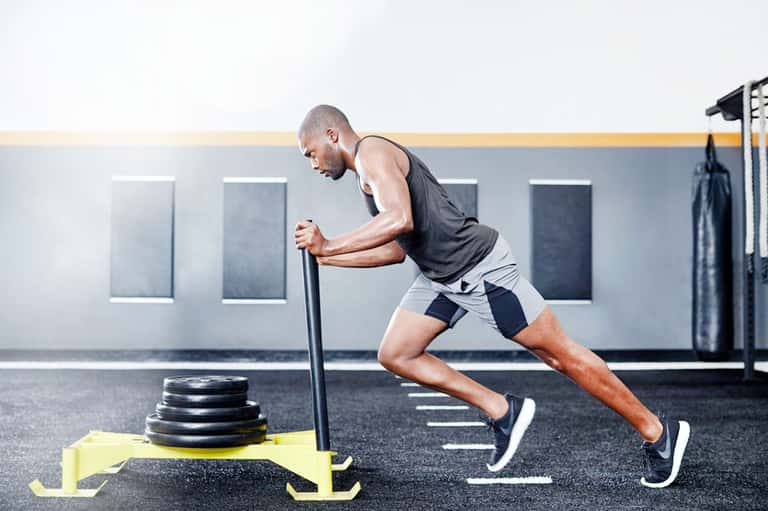 Man performing sled push exercise with weighted plates at a modern gym