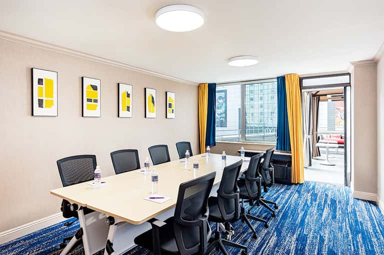 Modern conference room with long white table, black mesh chairs, blue curtains, and city views