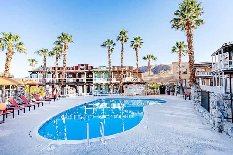 Resort pool with curved design, palm trees, western-style buildings, and desert mountain backdrop