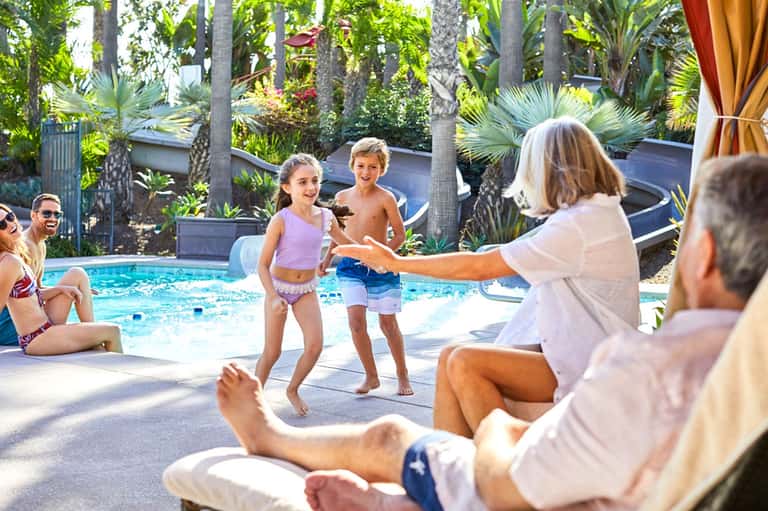 Family enjoying outdoor pool with children playing while adults supervise in tropical setting